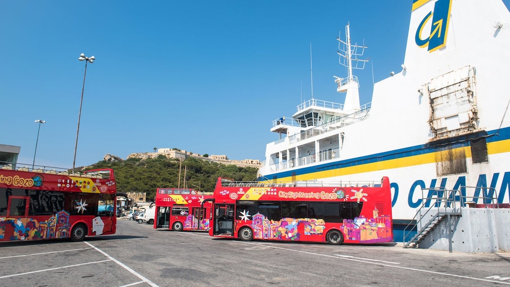 red double decked busses parked near a cruise ship in Gozo