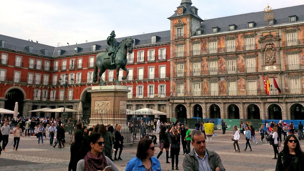 man on horse sculpture surrounded by passing crowds in Spain