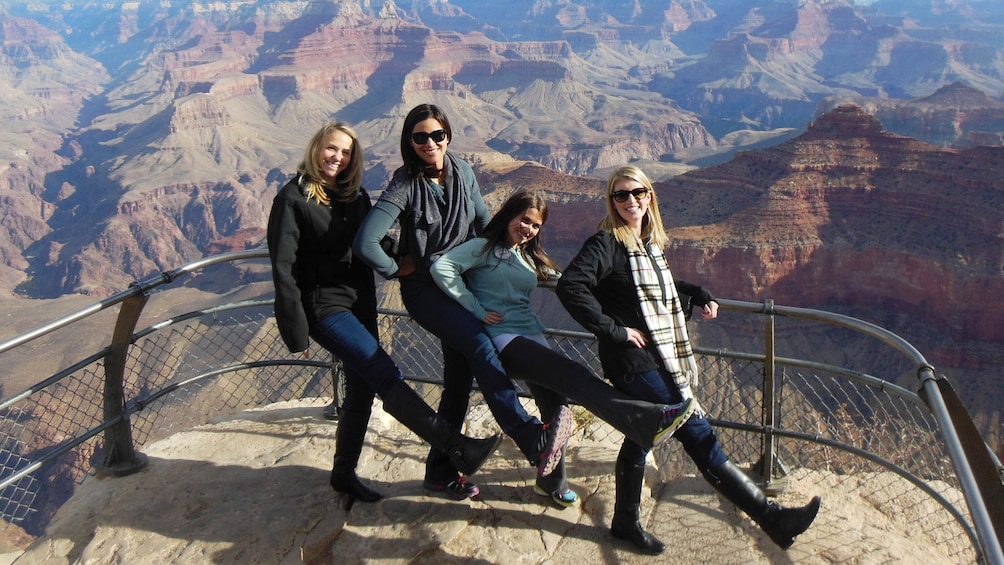 Four women holding their right legs out  on an observation deck at the Grand Canyon
