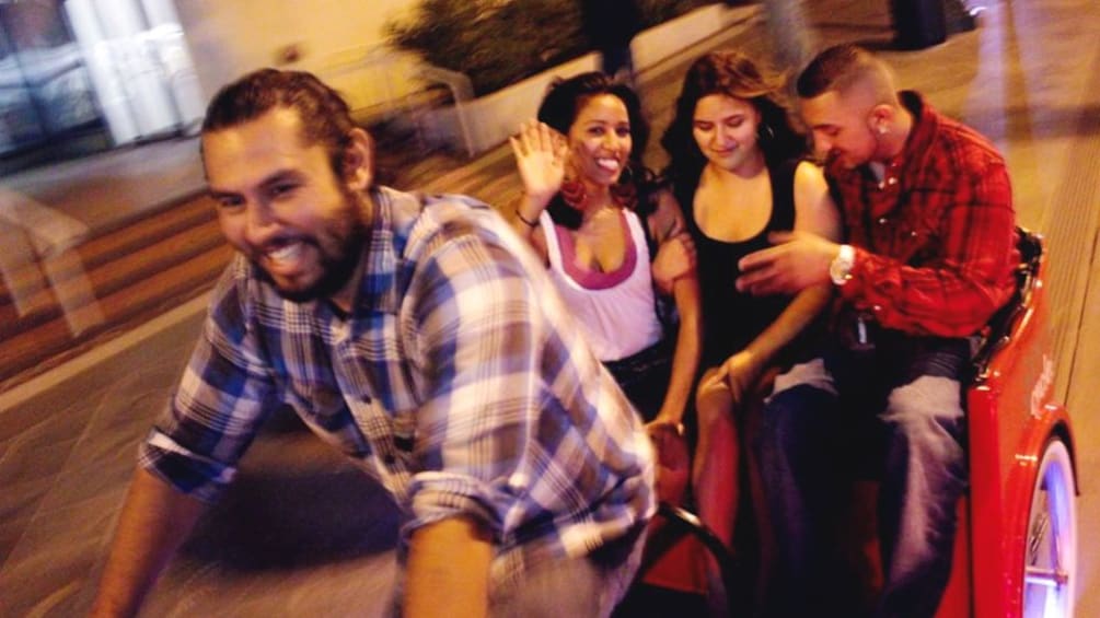 Group of young people traveling to pub by pedicab at night.