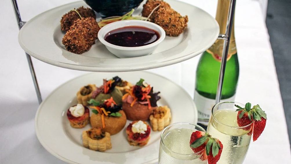 Small appetizers on white plates with bottle of champagne.