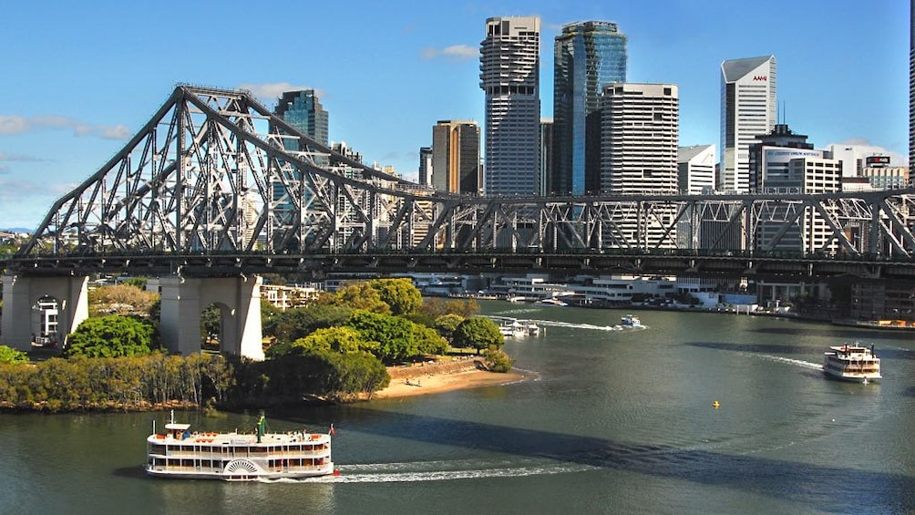 Cruise boats moving across water with view of bridge and city skyline.