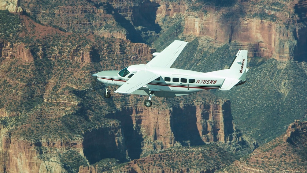 Small aircraft flying over Grand Canyon during the day.