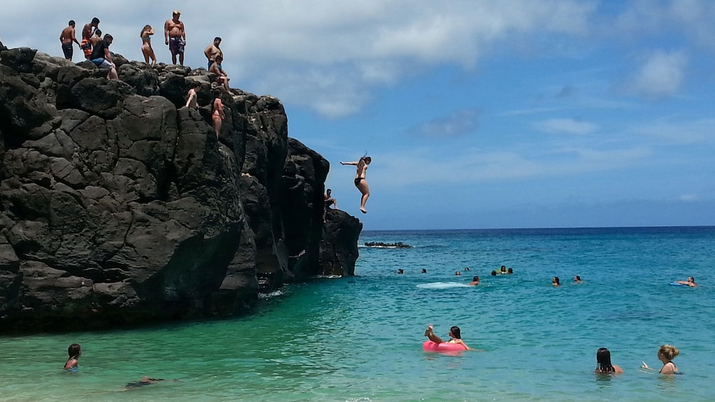 People jump from rocks into water in Oahu