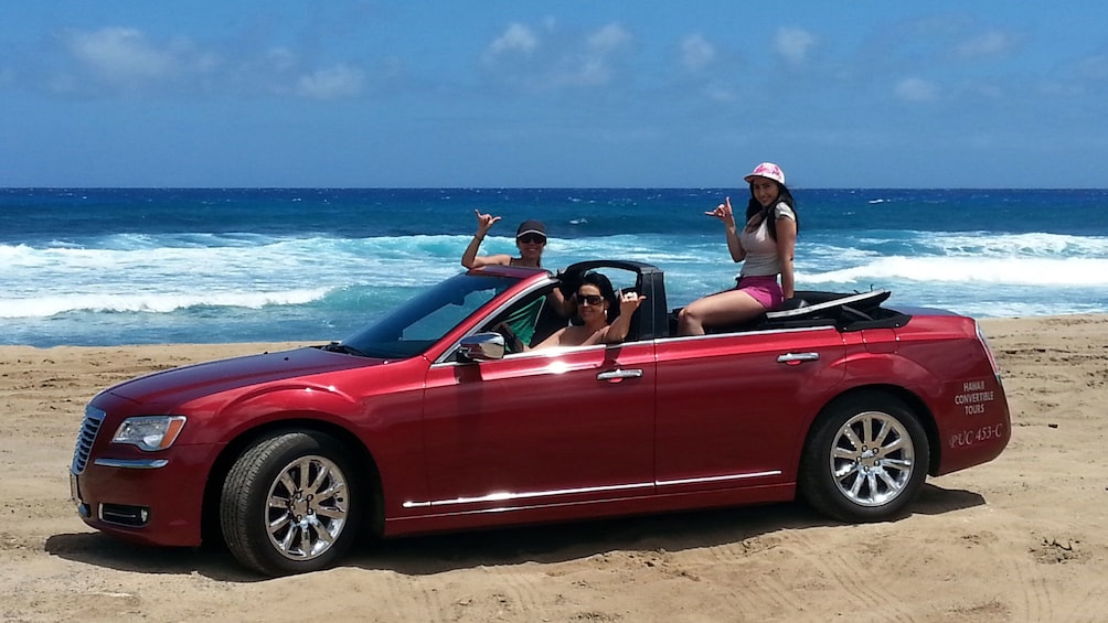 Three women posing in convertible on beach in Oahu