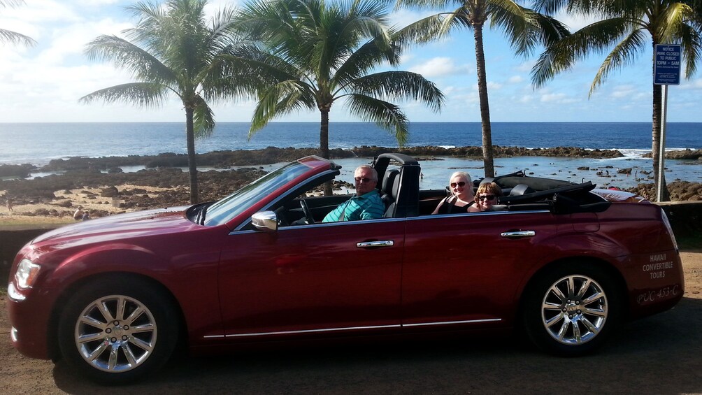 Three people sit in convertible near beach on Oahu