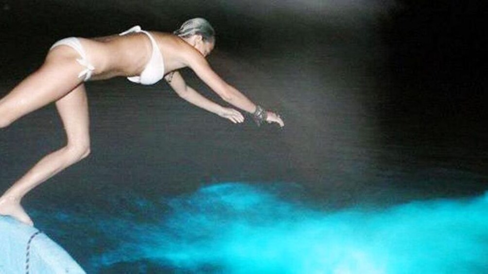 Show item 5 of 8. Woman jumping into water with Bioluminescence