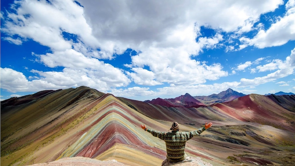 Hiking man sitting on a rock looking out at the colorful peaks of Rainbow Mountain in Lima