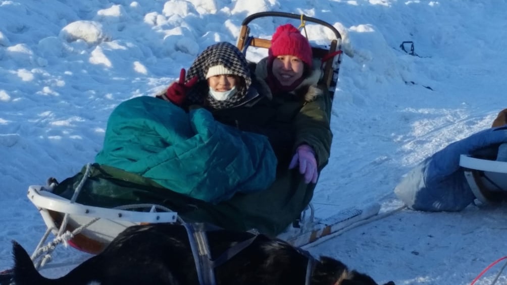 Pair of women bundled up in blankets on a sled in Alaska