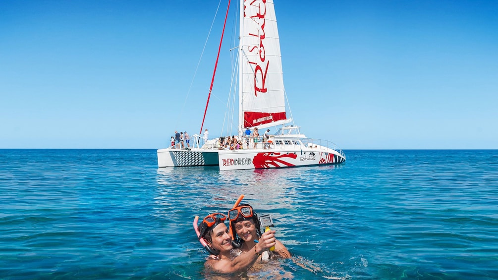 Two people swimming in the ocean next to a Catamaran in Jamaica