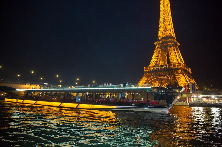 Night time view of a dinner cruise boat along the River Seine with the Eiffel Tower in the background 