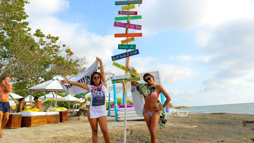 Two women stand next to a sign on a beach