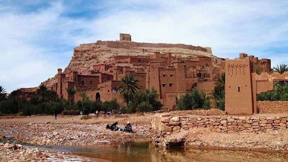 View of city by the river, people sitting near river edge in Ait Ben Haddou Kasbah