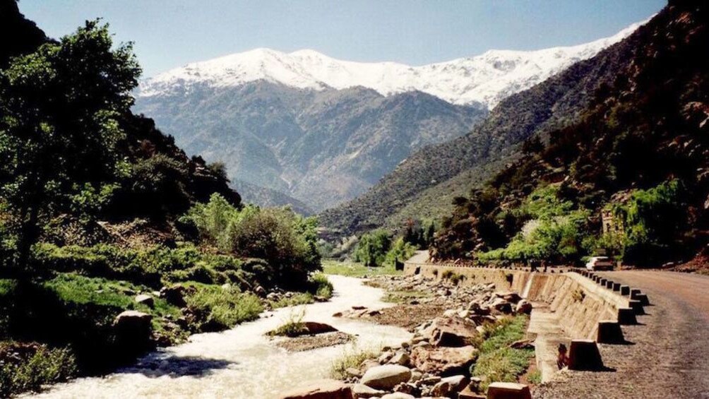 Road and greenery along river, mountains in background in 3 Valleys