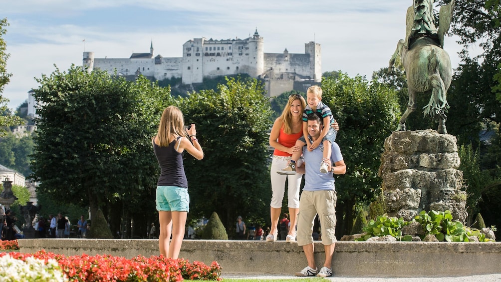 Show item 4 of 5. Family photo at a statue with castle a hill in the background in Salzburg