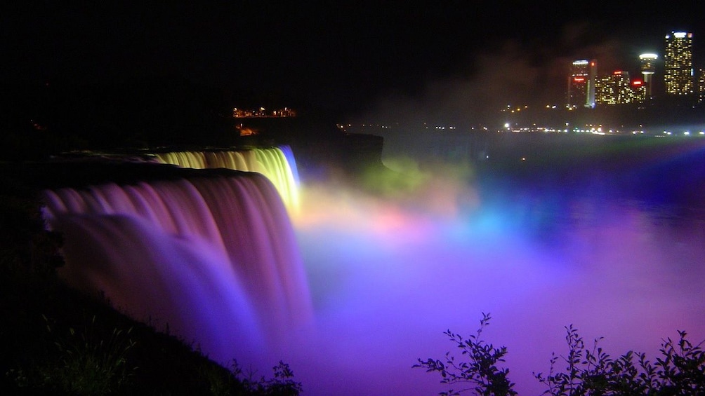 Niagara Falls lit up with different colored lights at night. 