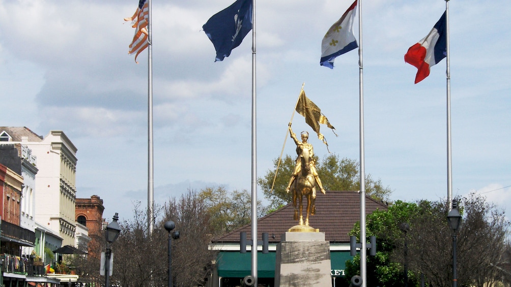Golden statue of Joan of Arc with flags flanking either side in New Orleans