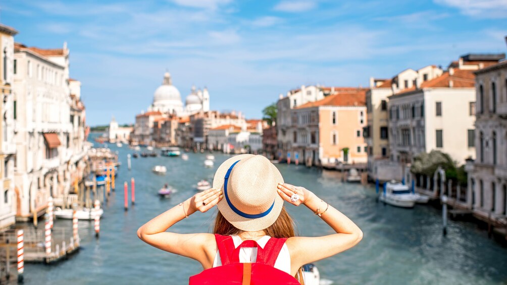 Tourist holding hat as she overlooks canal in Venice