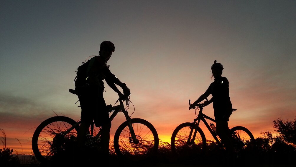 Mountain bikers siting on bikes as the sun sets on Table Mountain