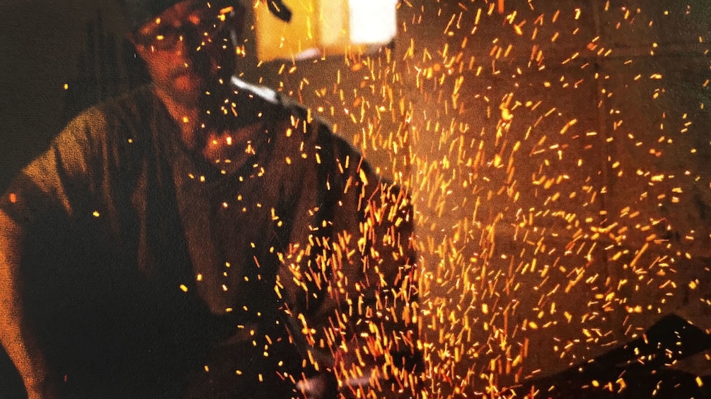 Embers fly as work is done on metal with the blacksmith in the background in Kyoto