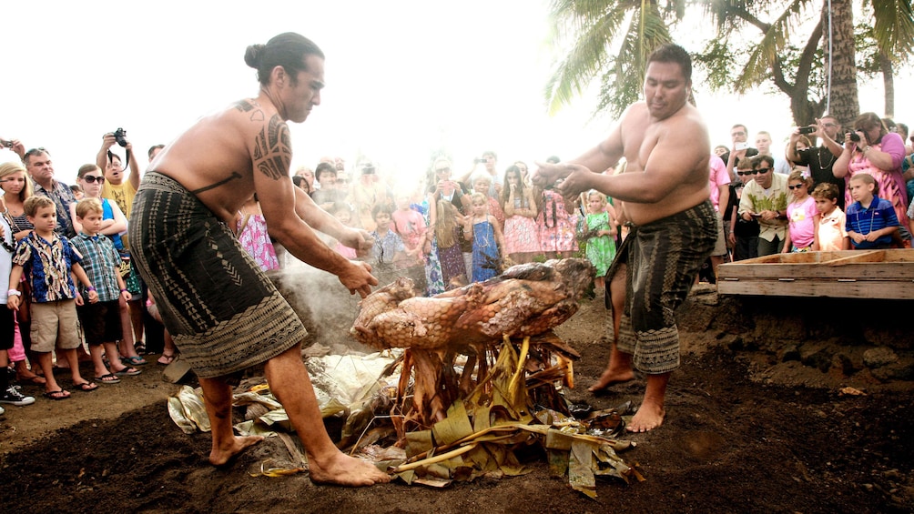 Show item 2 of 8. Two hawaiian men roasting a pig over a fire in Hawaii