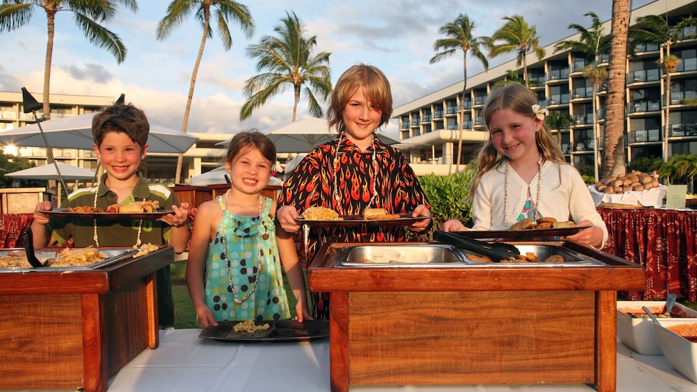 Show item 4 of 8. Group of kids getting plate of food at a luau in Hawaii