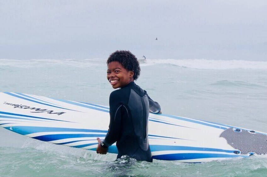 Boy smiles with surfboard.