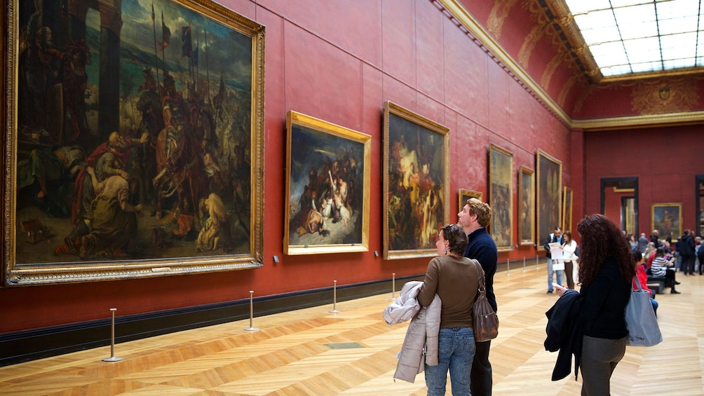 Tourist viewing large paintings in hall in the Louvre