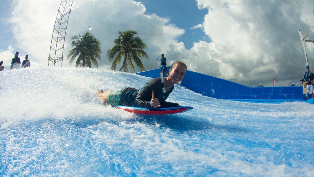 Woman giving hang loose sign as she rides the flowrider wave generator in Aquaworld Cancun