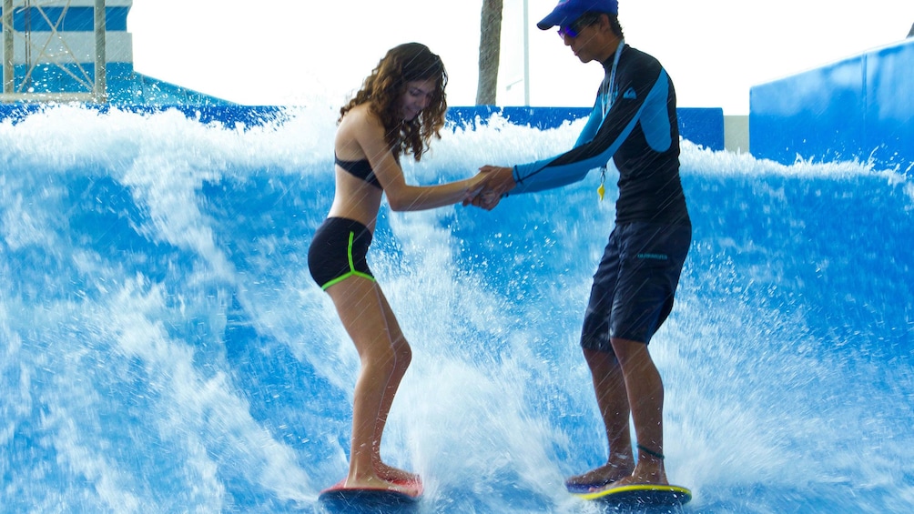 Woman holds hands with instructor as she rides the flowrider wave generator in Aquaworld Cancun
