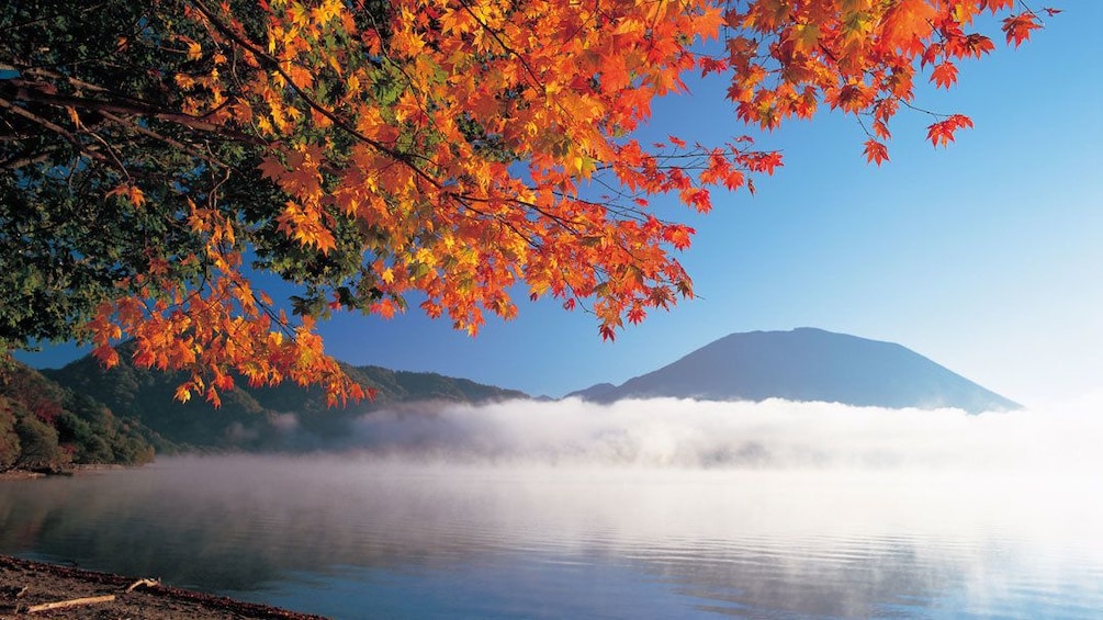 Fall colors on the trees as low lying clouds sit over the lake with mountain in background