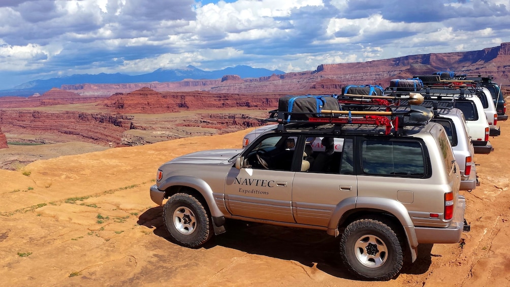 Fleet of 4x4 tour vehicles lined up by edge of cliff in White Rim, Moab