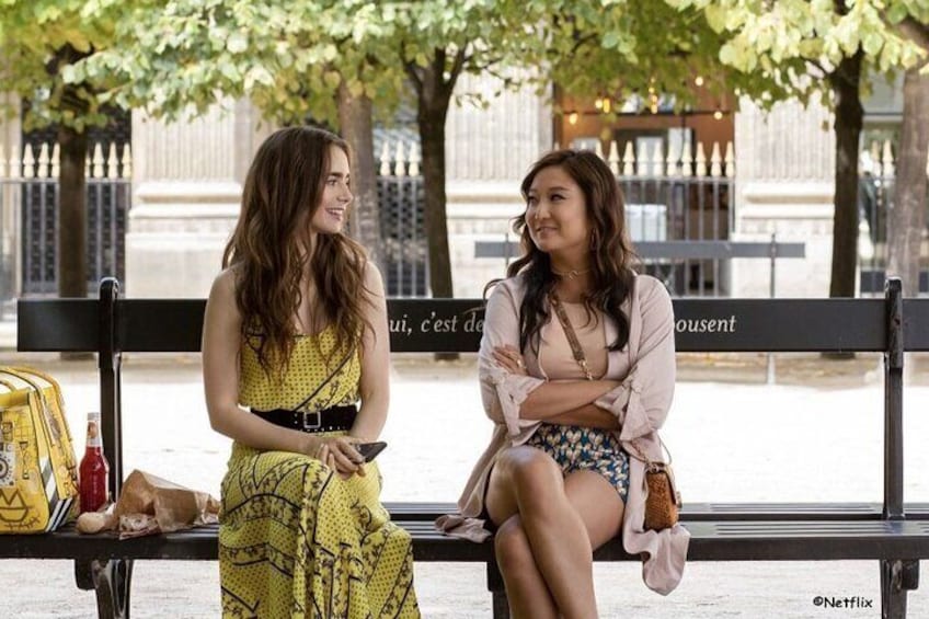 Emily talks on a bench with her friend Mindy in the garden of the Palais Royal