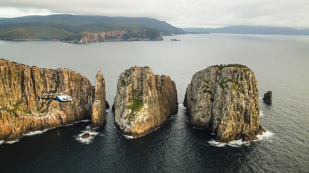 Show item 3 of 9. Helicopter flies near sea cliffs in Hobart