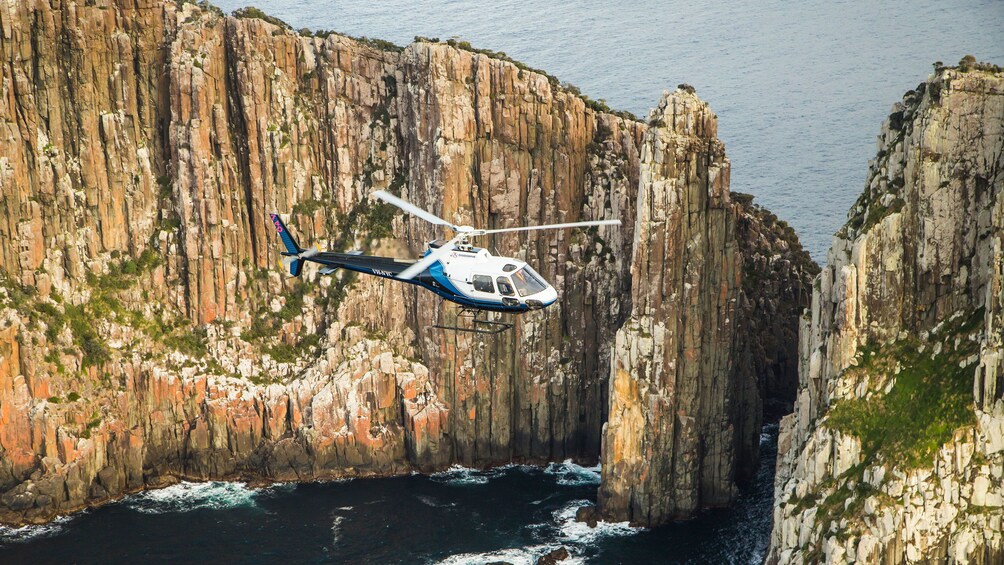 Show item 2 of 9. Close up of helicopter flying near sea cliffs in Hobart