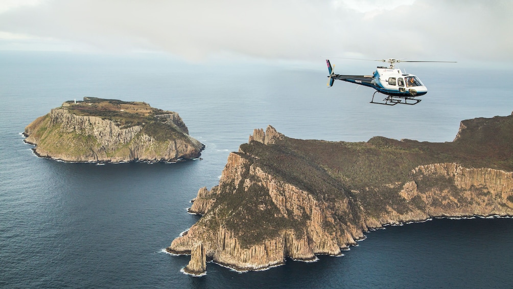 Show item 4 of 10. Helicopter flys near cliffs of Tasman Island