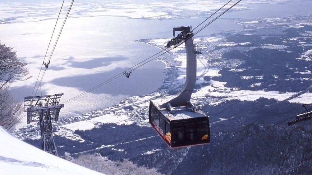 Large gondolas traveling up mountain with lowlands in background at Biwako Valley Ski Resort