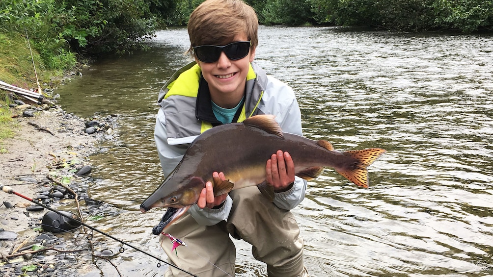 Young fisherman holds up salmon in Denali National Park