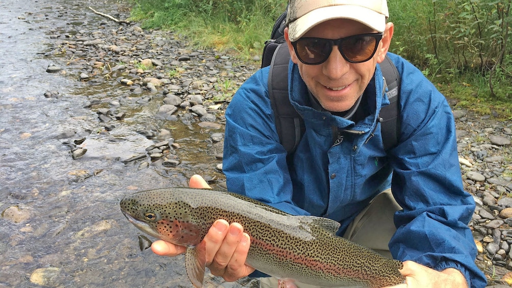 Man holding a freshly caught fish on the Jet Boat Fishing Trip in Denali National Park, AK