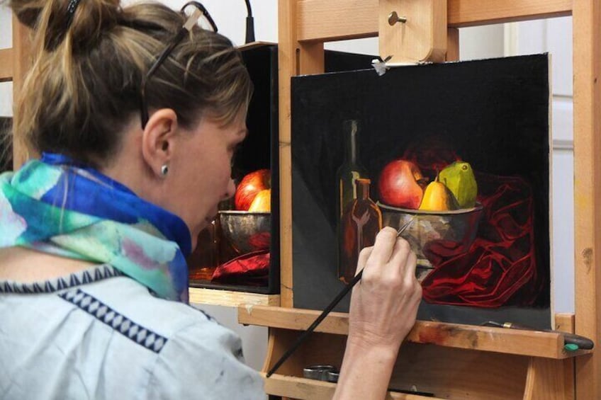 A student painting a classical fruit still life.