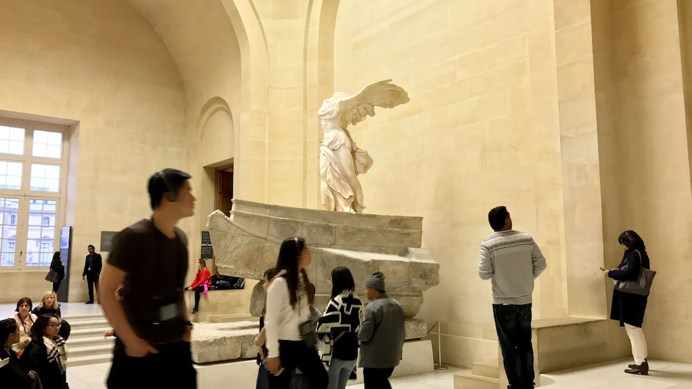 People walking up stairs past sculpture in the Louvre Museum in Paris