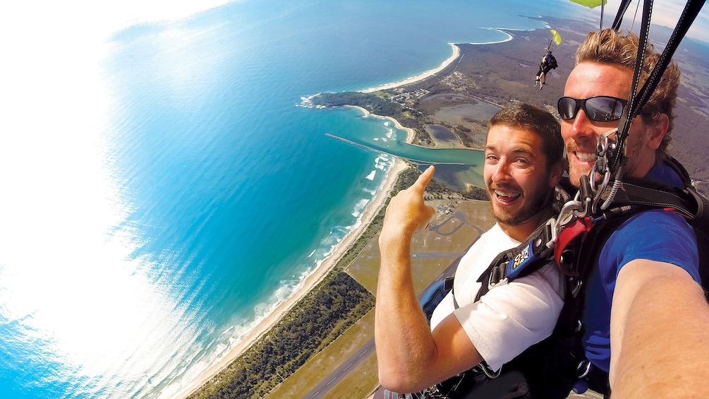 Skydivers with parachute deployed point out other skydivers over Batemans Bay