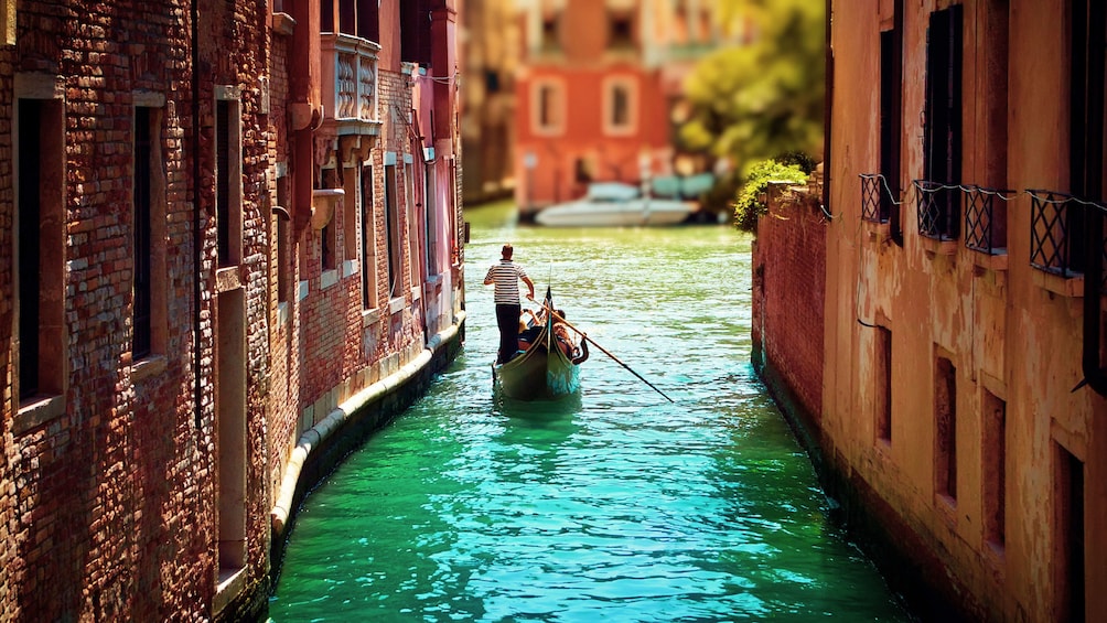 Single gondola paddles down narrow waterway in Venice