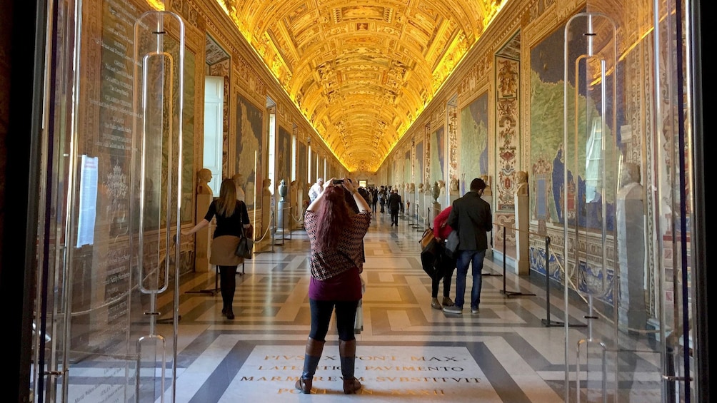 Woman taking photo of long ornately decorated hallway at the Vatican