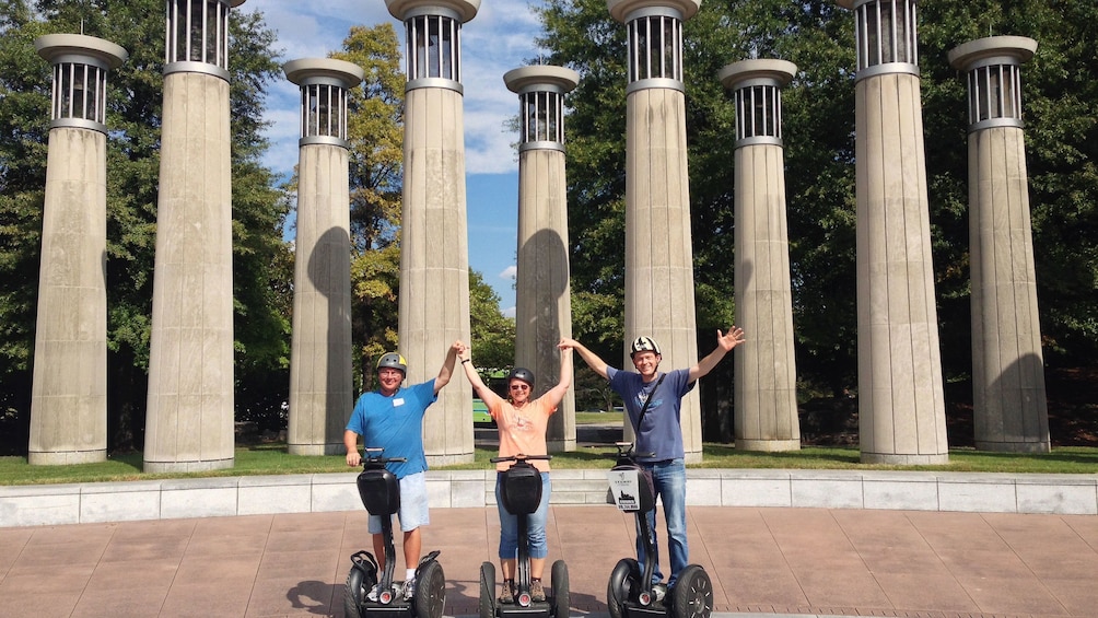 Three segway riders pose for photo in front of columns in park on tour of Nashville