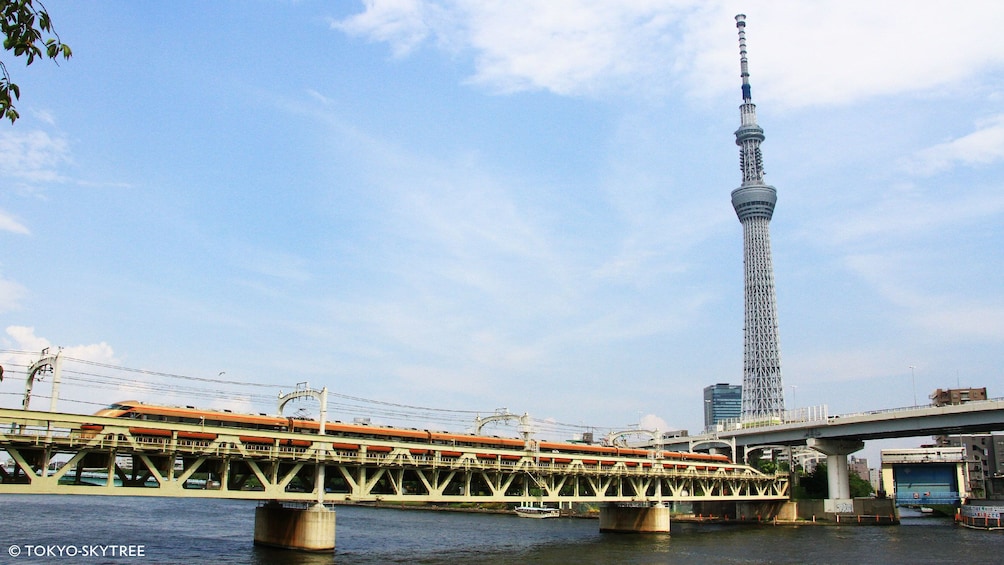 Show item 4 of 5. View of Skytree from river with train traveling by in Tokyo