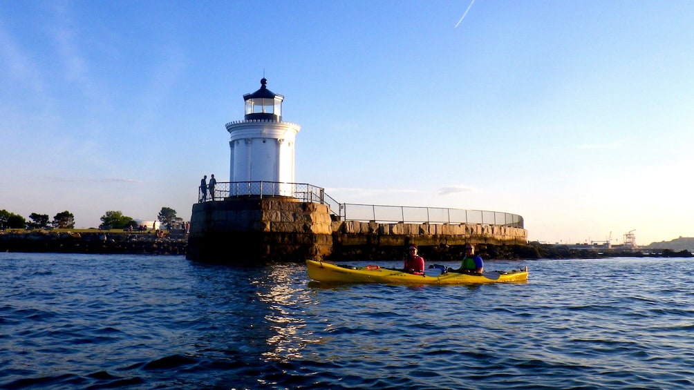 Kayaking pair passing a lighthouse at Casco Bay