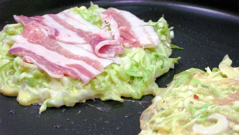 Tasty Okonomiyaki being fried on a pan at the Osaka Cooking Class in Osaka, Japan