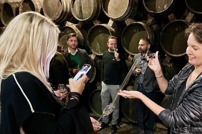 Bodega Mallorca premium tasting tour in Palma in Majorca. Aged brandy is extracted directly from the cask and served into the glass of the visitors to taste exclusive spirits. Groups of women and men.