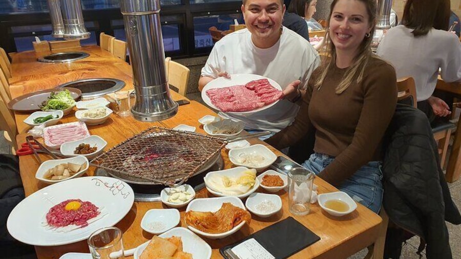 A happy couple enjoying premium Hanwoo beef at Majang Meat Market. Their table is filled with fresh cuts, vibrant side dishes, and traditional Korean flavors ready for grilling!